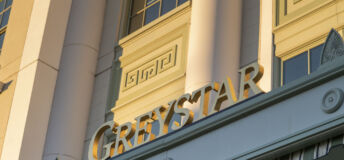 Greystar's logo on the facade of its office, illuminated by sunlight at sunset.